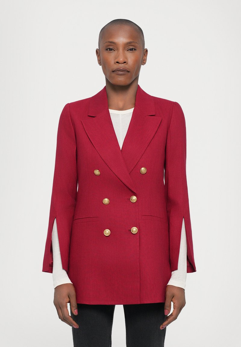 Red double-breasted blazer with gold buttons, featuring a structured design, side slits, and smooth texture, paired with a white top underneath.