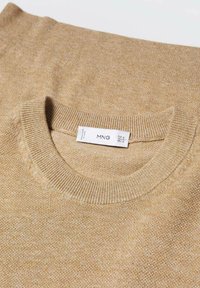 Pull en maille beige avec un col rond, doté de poignets et d'un ourlet côtelés. Le tissu a une texture douce avec un motif subtil. Étiquette de la marque visible.