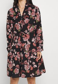 Černé květinové šaty s dlouhými rukávy, stahováním v pase a sukni ve vrstveném provedení. Tkanina má strukturovaný povrch s růžovými a bílými květinovými vzory.