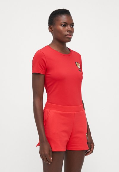 T-shirt rossa in cotone con maniche corte e colletto rotondo, con una grafica di un orso sul petto sinistro, abbinata a pantaloni corti coordinati.