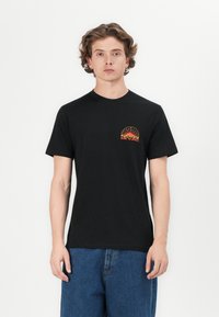 Sort bomulds-T-shirt med rund halsudskæring og korte ærmer, prydet med et farverigt "RIP CURL" solnedgangsdesign på venstre bryst.