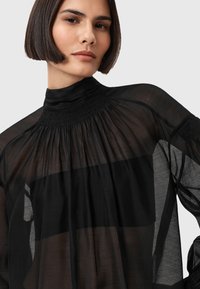Blusa nera trasparente a maniche lunghe con colletto alto, pieghe arricciate al collo e vestibilità ampia con tessuto fluido.