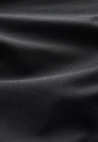 Tissu noir lisse avec des plis doux et des reflets subtils, montrant la texture et des reflets lumineux délicats.