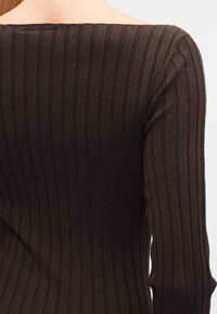 Brun ribbestrikket genser med bred utringning og lange ermer, med teksturert stoff og vertikalt stripemønster.