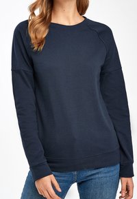 Sweatshirt bleu marine en tissu doux avec un col ras du cou, des manches longues et des poignets côtelés. Présente un design simple et épuré.