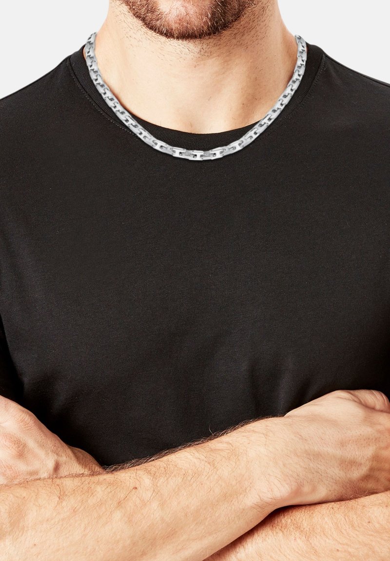 Zwarte t-shirt met een zilveren kettinghalsband. De ketting heeft een vlak, rechthoekig schakeldesign, wat een contrasterende textuur oplevert met de gladde stof.