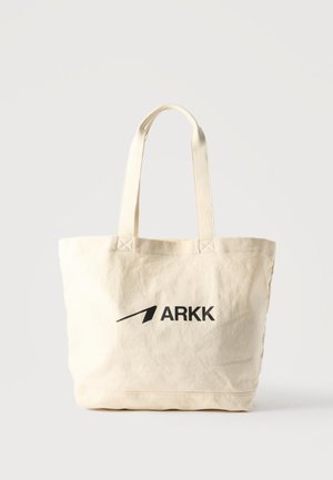 Geantă tote din pânză bej cu două mânere și logo-ul negru „ARKK” imprimat pe față, așezată pe un fundal alb.