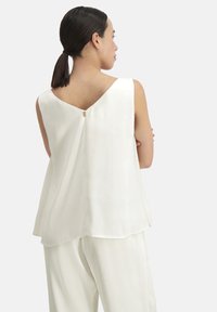 Witte mouwloze top met een V-vormige achterkant, gladde textuur en een klein centraal ritsdetail. Gecombineerd met bijpassende comfortabele broek.