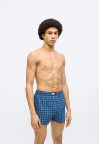 Μπλε καρό μποξεράκια με ελαστική μέση, που διαθέτουν μια μικρή ετικέτα με λογότυπο. Το ύφασμα έχει λεία υφή και άνετη εφαρμογή.