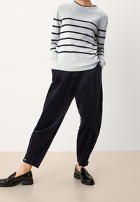 Hellgrau gestreifter Pullover mit navyblauen horizontalen Streifen, kombiniert mit dunkelblauen strukturierten Hosen und glänzenden schwarzen Slippern. Entspannte Passform.