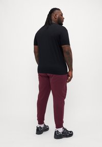 Tricou negru cu mânecă scurtă, pantaloni jogger căpșunii și încălțăminte sport neagră cu accente albe. Păr texturat coafat în codițe.