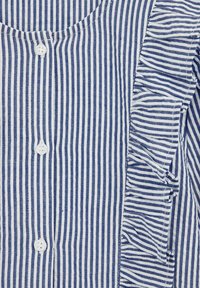 Mėlynos ir baltos juostelės marškiniai su mygtukais, vienoje pusėje apipavidalinti volanais, su apvaliu iškirpimu, pagaminti iš lengvos medžiagos.