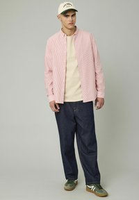 Chemise à rayures rouges et blanches, accompagnée d'un t-shirt beige, de jeans foncés à coupe large et de baskets vertes avec des accents blancs.