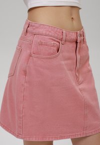 Et rosa denimskjørt med tettsittende midje, A-linje-form, glidelås foran og lommer, med teksturert stoff og synlige sømdetaljer.
