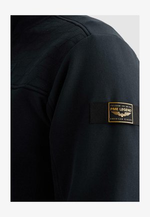 Črna majica z dolgimi rokavi, ki ima prešite detajle na rami in črno nalepko z zlatim logotipom "PME Legend American Classic" na rokavu.