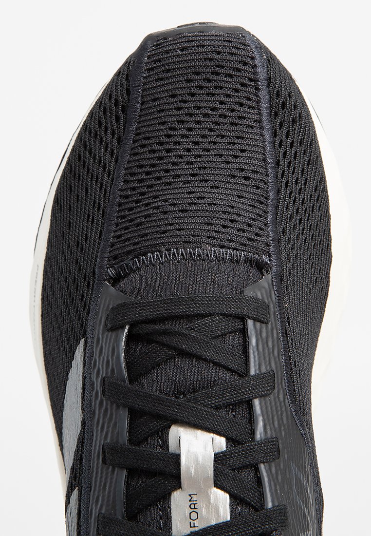 Schwarzer Sportschuh mit einem strukturierten Mesh-Obermaterial, reflektierenden Akzenten und einer weißen Zwischensohle. Verfügt über schwarze Schnürsenkel und ein schlankes Design.