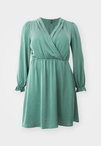 Vihreä kietaisumekko, joka on valmistettu sileästä kankaasta. Tässä mekossa on pitkät hihat joustavilla hihansuilla, V-pääntie sekä vyötäröllä istuva malli, joka laskeutuu levenevänä hameena.