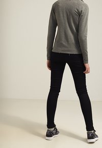 Šedé tričko s dlouhým rukávem, černé slim fit kalhoty a vzorované tenisky. Tričko má švový detail na zadní straně a přiléhavý střih.