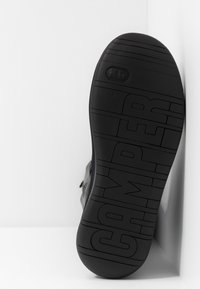 Suola di scarpa in gomma nera con un evidente motivo di battistrada e logo "CAMper". Superficie testurizzata, bordi arrotondati e design minimalista.