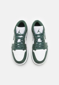 Paire de baskets basses blanches et vert foncé avec boîte à orteils perforée et logo sur la languette, vues de dessus sur fond blanc.