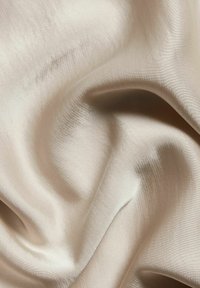 Harmaanbeige satiinikangas, jossa on sileä ja kiiltävä pinta, pehmeät laskokset ja hienovarainen tekstuuri, heijastaen valoa tyylikkäästi.