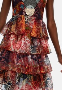 Robe à motif floral, en couches, en tissu transparent multicolore avec des ourlets froncés. Dotée d'un col décoratif en perles.