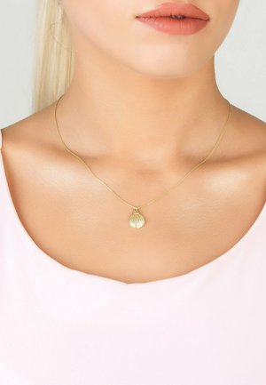 Collier en pendentif en coquillage doré sur une chaîne délicate, avec une texture nervurée et une finition polie, porté sur une peau nue.