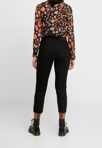Black skinny jeans with a high waist, featuring a frayed hem. Paired with a floral long-sleeve blouse in dark colors and black lace-up boots.