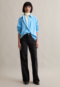 Light blue button-up shirt with rolled sleeves, paired with high-waisted black denim pants, featuring a relaxed fit and textured fabric.