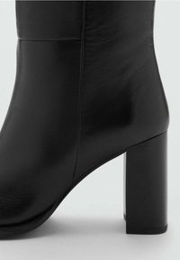 Bottine en cuir noir avec talon bloc cylindrique. Texture lisse, design ajusté avec des détails de couture minimaux.