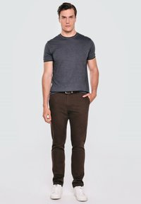 Šedé tričko s krátkým rukávem v kombinaci s tmavě hnědými kalhotami a bílými teniskami. Oblečení má jednoduchý design a klasický střih.