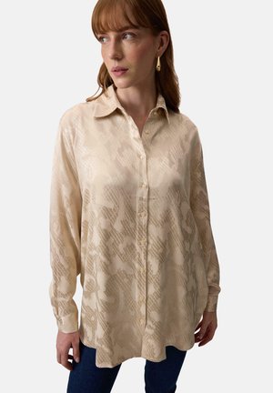 Beige long-sleeve shirt with a textured, patterned finish. Features a button-down front, relaxed fit, and classic collar. Casual design.