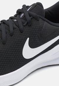 Črne atletske čevlje iz mrežaste in sintetične snovi. Imajo bel Nike žig in strukturirane črne detajle. Bele podplat.