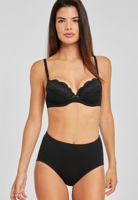 Melnas mežģīņu krūšturis ar polsterētām krūšu kausām, viļņotām malām un regulējamām siksnām, apvienots ar melnām kokvilnas biksēm ar augstu jostasvietu.