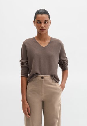 Brown V-neck sweater with rolled sleeves, paired with light beige high-waisted pants featuring a button closure and side pockets.