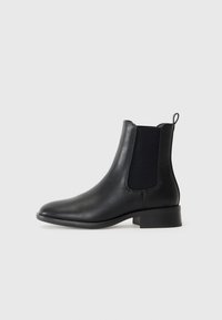 Botas de cuero negro hasta el tobillo con paneles laterales elásticos, punta redondeada y un tacón bajo. Presenta un tirador en la parte posterior.