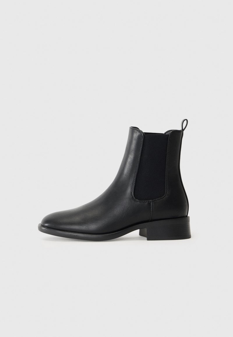 Botas de cuero negro hasta el tobillo con paneles laterales elásticos, punta redondeada y un tacón bajo. Presenta un tirador en la parte posterior.