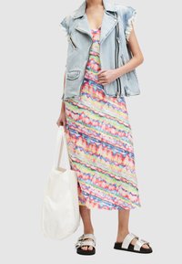 Veste sans manches en denim avec des bords effilochés sur une robe maxi tie-dye colorée. Comprend un sac fourre-tout blanc et des sandales argentées à boucles.