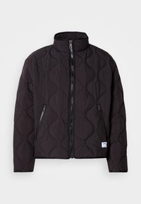 Black quilted jacket with wavy stitch pattern, front zipper, two zippered side pockets, and a small white brand label near the hem.
