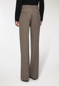 Pantaloni beige su misura con vita alta, gamba larga e due tasche posteriori con chiusura a bottone, realizzati in tessuto morbido.