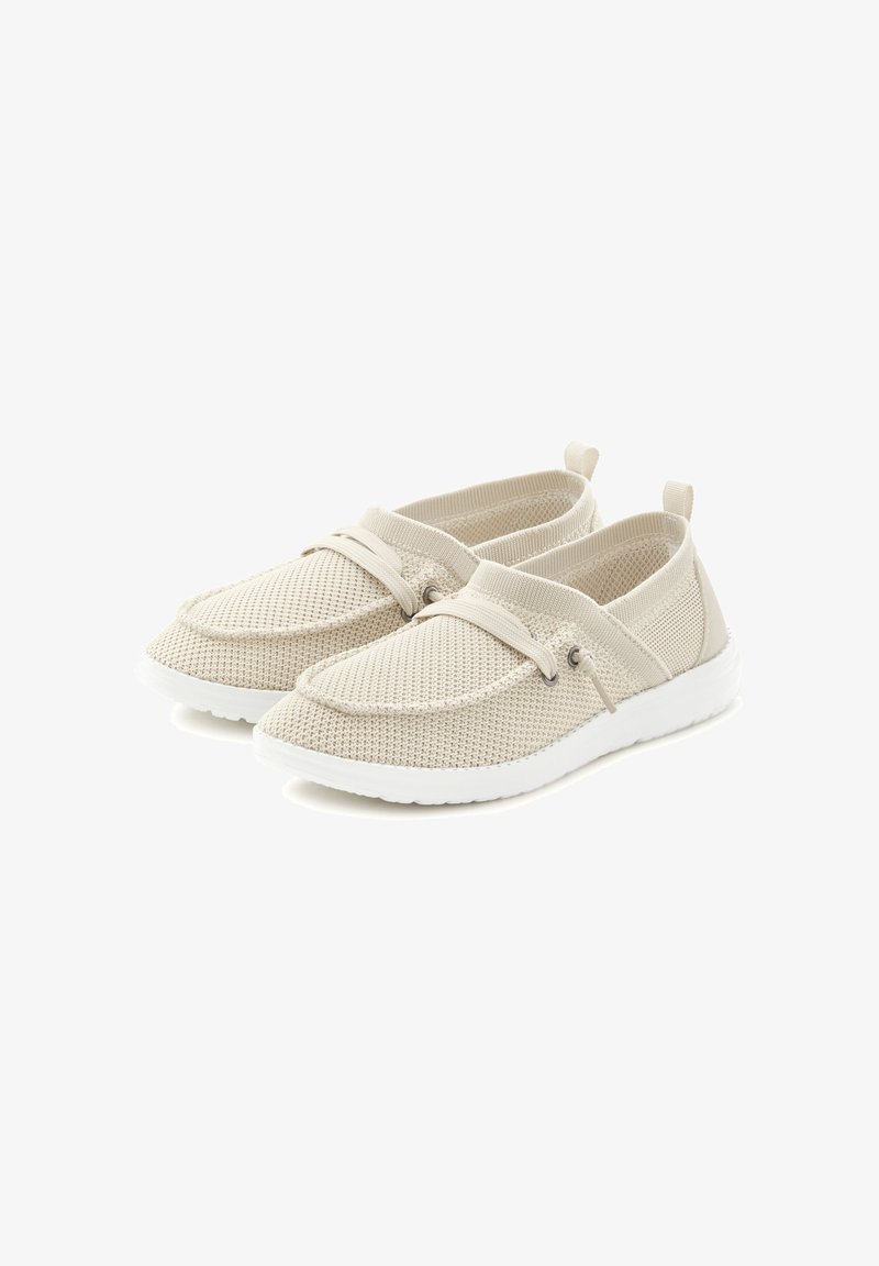 Gaiši bēša sieta zābaci ar baltu gumijas zoli, kas aprīkoti ar elastīgām siksnām pāri augšai un dekoratīvām aparatūras akcentiem.