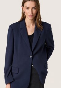 Marineblå blazer med en enkelt knaplukning, notch-lommer og to forlommer. Glat stof med en afslappet pasform.
