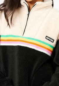 Fleece-Pullover mit einem Viertelreißverschluss, ausgestattet mit einem beigen oberen Teil, einem schwarzen unteren Teil und einem mehrfarbigen gestreiften Band über der Brust. Markenlogo sichtbar.