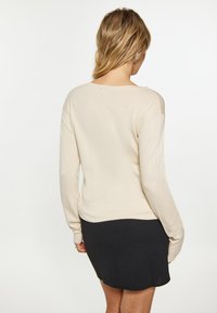 Rundhalspullover in hellem Beige, aus weichem Stoff, mit langen Ärmeln. Kombiniert mit einem eng anliegenden schwarzen Rock, der eine glatte Textur und ein schlichtes Design aufweist.