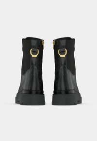 Czarne botki za kostkę o błyszczącym wykończeniu, z akcentami złotego hardware'u i masywną podeszwą. Posiadają zamki błyskawiczne i detal w postaci pętli z tyłu.