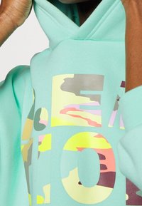 Felpa verde menta con motivo camouflage in tonalità di rosa, giallo e grigio. Include una grande stampa grafica sul davanti.