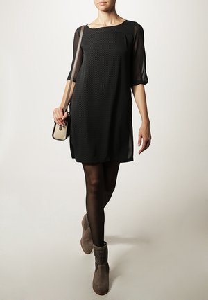Robe noire avec des manches transparentes, col rond et tissu texturé. Assortie à des bottines grises et un petit sac bandoulière.