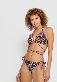 Bikini komplekts ar purpura, oranžām un melnām ģeometriskām krāsām. Iezīmē trīsstūra augšdaļu ar krusteniskām siksnām un saitējamām biksēm.