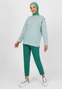 Maglietta bianca a maniche lunghe con righe verdi, abbinata a pantaloni slim-fit verdi e sneakers bianche con dettagli verdi. Modello che indossa un hijab verde.