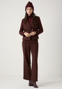 Burgunderfarbener karierten Anzug mit einem maßgeschneiderten Blazer und weitem Hosen, kombiniert mit einer passenden gestrickten Mütze und dunklen Stiefeletten.